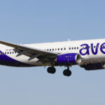 An Avelo Airlines B737 mid-flight, its logo on clear display and a bright blue sky in the background.
