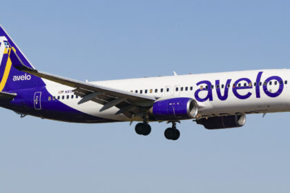 An Avelo Airlines B737 mid-flight, its logo on clear display and a bright blue sky in the background.