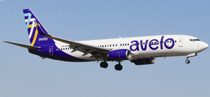 An Avelo Airlines B737 mid-flight, its logo on clear display and a bright blue sky in the background.