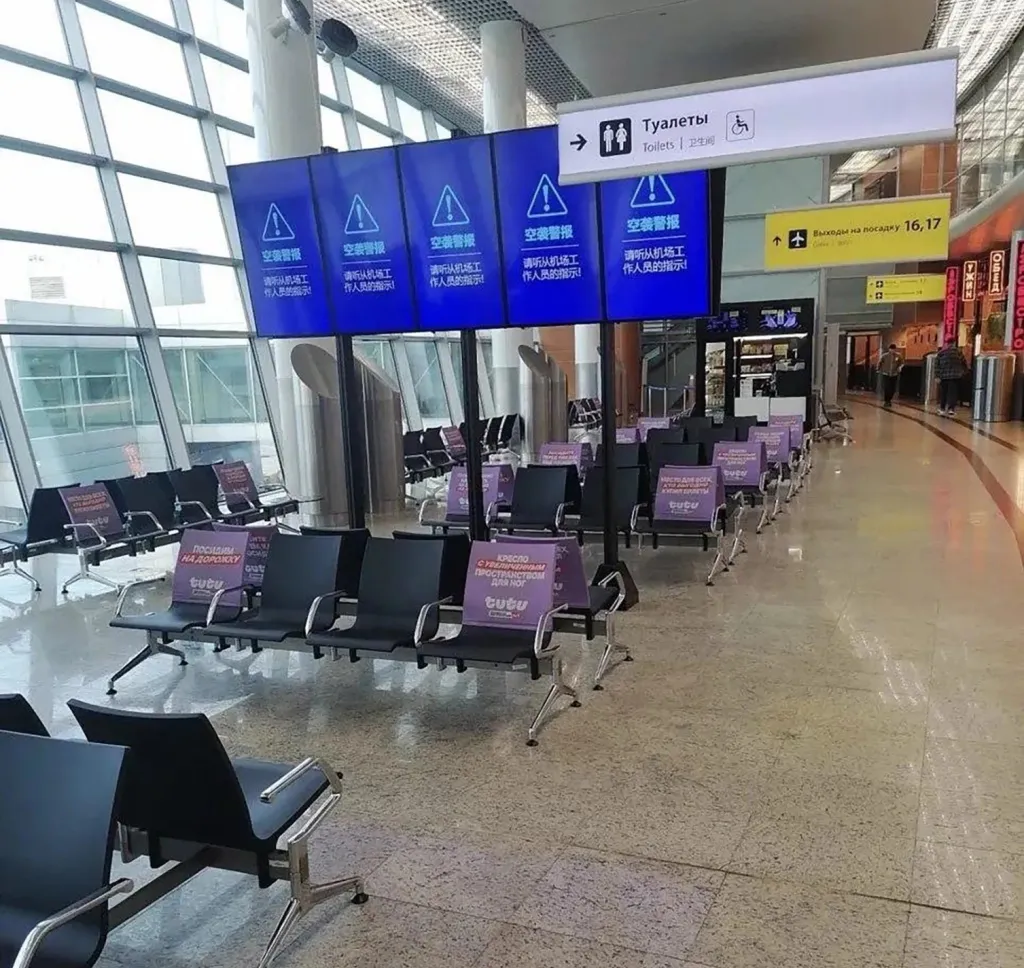 Empty terminal at a Moscow airport where travellers were evacuated from terminals and herded into bomb shelters. The seats are all empty and there are warning signs on all the screens.