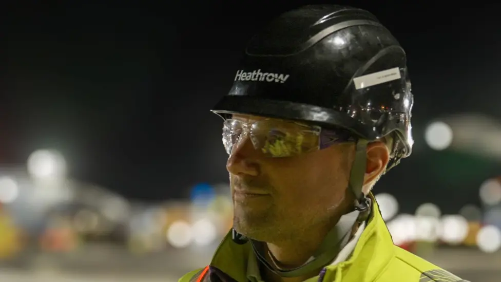 Image shows a close-up of Alistair Awcock, Heathrow's infrastructure delivery and strategic planning director at night wearing a safety helmet and equipment