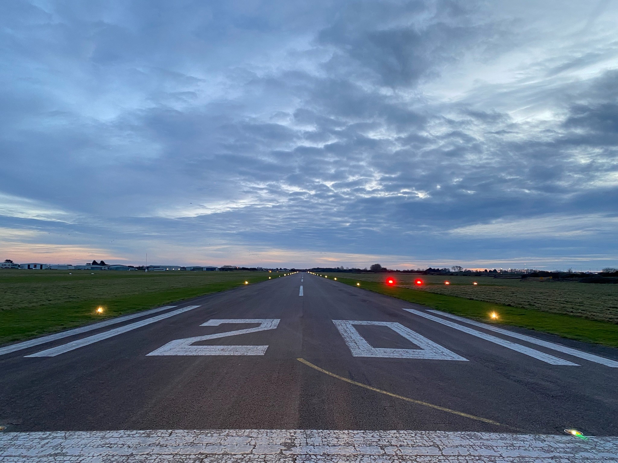 Image shows BCA's runway lit up at in a dusky cloudy sky with the number 20 visible and white lines to the edges of the runway