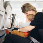 A mother sat in an airplane seat with a young child on her lap facing away from her.