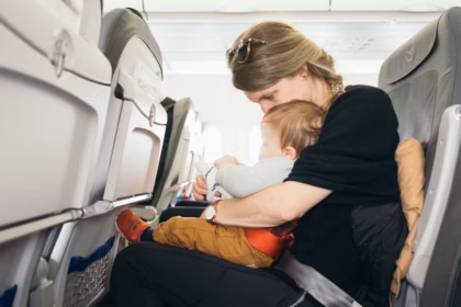 A mother sat in an airplane seat with a young child on her lap facing away from her.