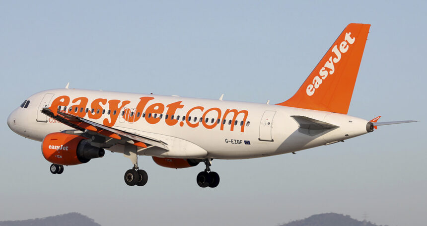 An easyJet Airbus A319 mid-flight with a blue sky in the background. The tips of two mountains can be seen in the distance.