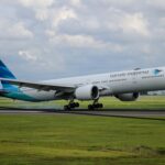 Garuda Indonesia plane getting reading for take-off with a field of green grass around it