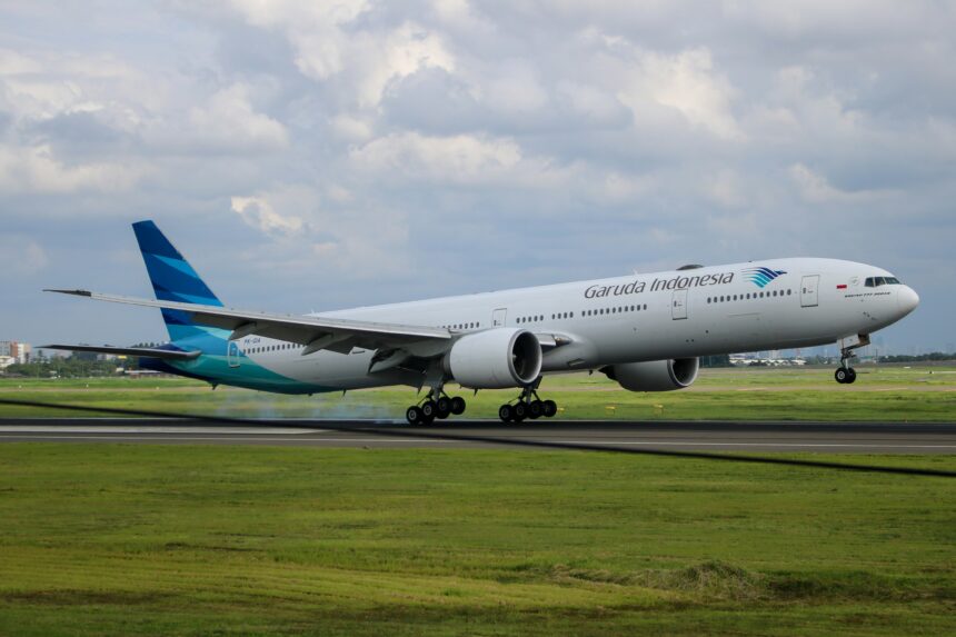 Garuda Indonesia plane getting reading for take-off with a field of green grass around it