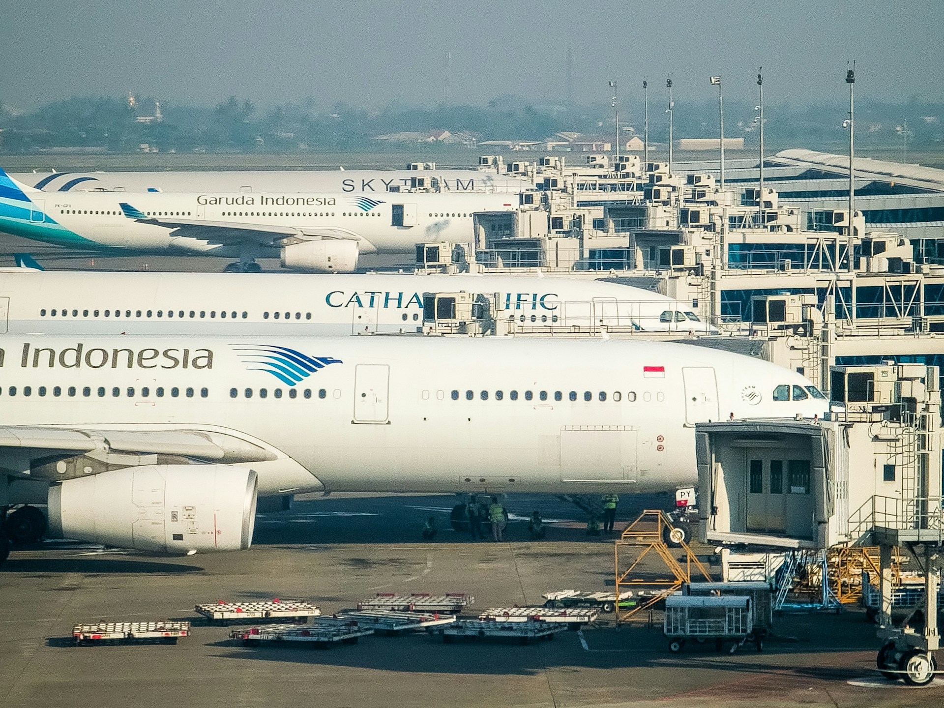 Air Indonesia aircraft is pictured on tarmac at an airport gate. There is a row of three other aircraft behind it, with a hazy blue sky in the background.