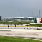 Felipe Ángeles International Airport (AIFA) terminal stands beyond a landscaped area, with large green, white and red letters on a mound under a grey, overcast sky.