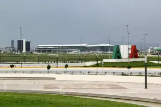 Felipe Ángeles International Airport (AIFA) terminal stands beyond a landscaped area, with large green, white and red letters on a mound under a grey, overcast sky.