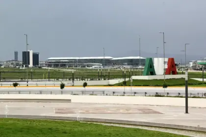 Felipe Ángeles International Airport (AIFA) terminal stands beyond a landscaped area, with large green, white and red letters on a mound under a grey, overcast sky.