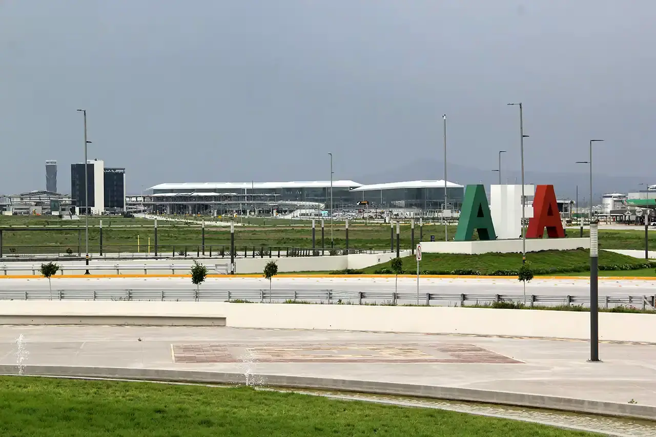 Felipe Ángeles International Airport (AIFA) terminal stands beyond a landscaped area, with large green, white and red letters on a mound under a grey, overcast sky.