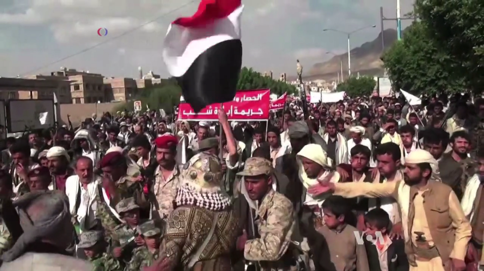 Houthis rebels can be seen protesting with a large group of people gathered together holding up signs and flags.