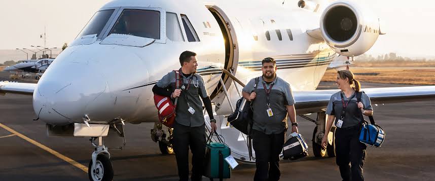 Three healthcare workers carrying supplies exiting an AirLink air ambulance.