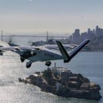 An Archer electric aircraft with tail number N703AX flies over Alcatraz Island with the San Francisco skyline and Bay Bridge visible in the background.