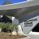 The modern, curved metal exterior of the Hollywood Burbank Airport terminal, featuring large black lettering against a gray, textured wall surface.