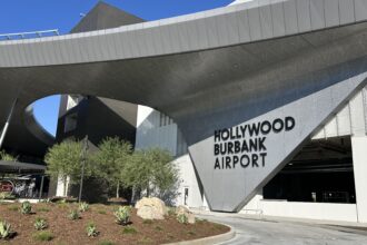 The modern, curved metal exterior of the Hollywood Burbank Airport terminal, featuring large black lettering against a gray, textured wall surface.