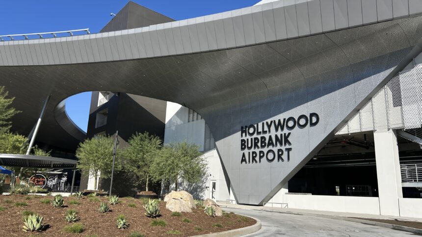 The modern, curved metal exterior of the Hollywood Burbank Airport terminal, featuring large black lettering against a gray, textured wall surface.