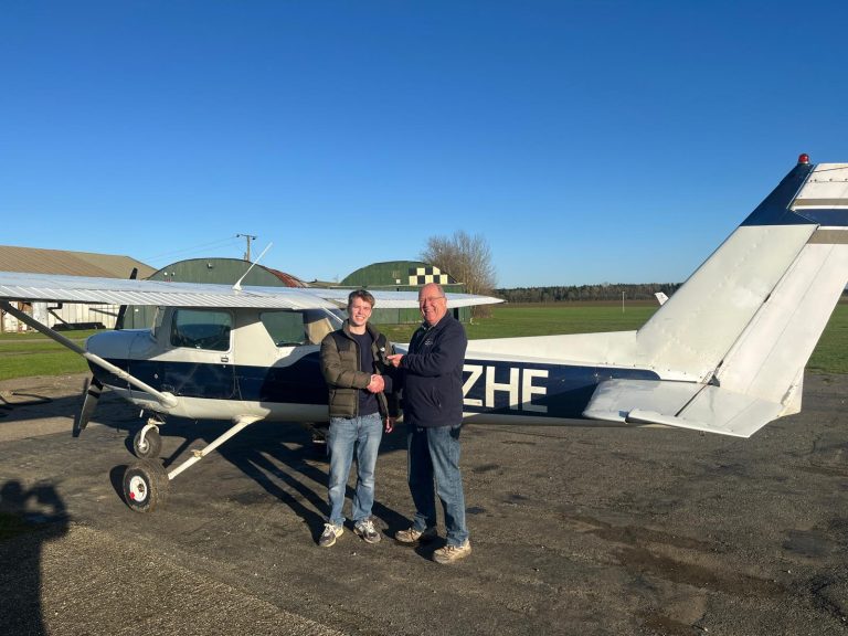 Andrewsfield Aviation student Josh Toms pass first PPL in 2025. The student and a member of the Andrewsfield Aviation team is stood in front of a small aircraft on in an open field.