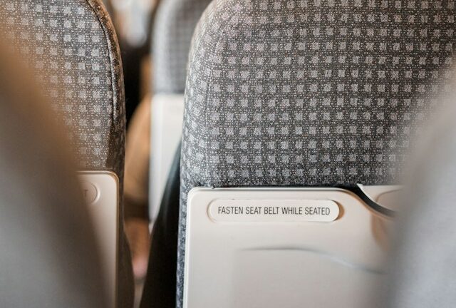 The back of an airplane seat with a reminder to fasten seat belt while seated.