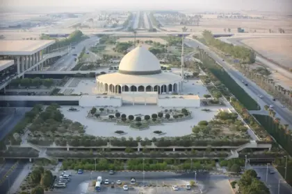 An ariel shot of King Fahd International Airport in Dammam, Saudi Arabia. A white building is at the centre of the area with a dome-shaped roof, its surrounded by areas of foliage and roads that run past other buildings.