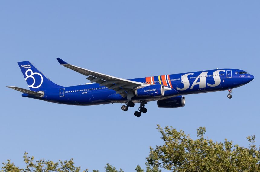 A dark blue SAS Airbus A330-343 during take off, with its landing gear extended above trees against a clear blue sky.