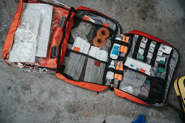 An open orange medical bag with supplies inside over a grey concrete floor 