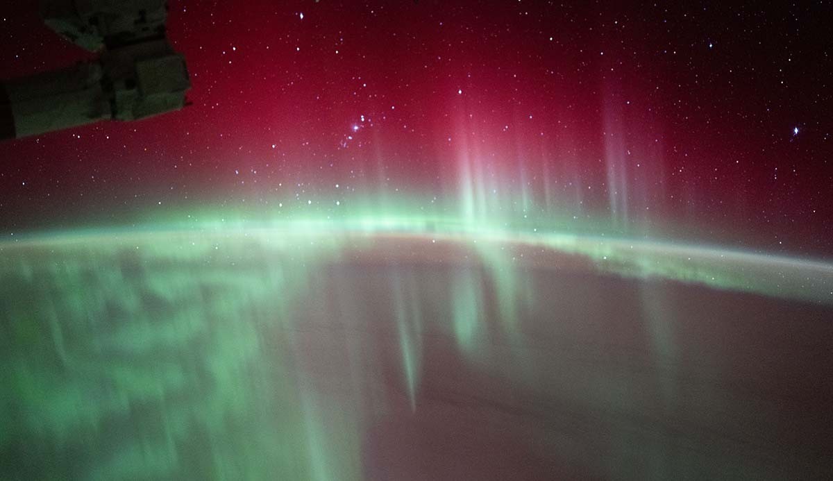 Image shows colourful green and pink northern lights in a starry sky hundreds of kilometres above the earth from the International Space Station 