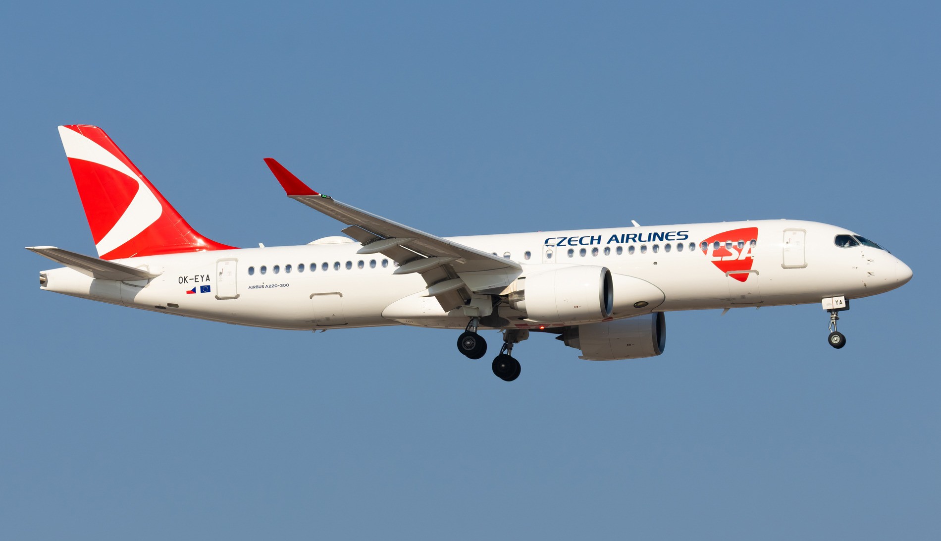 Czech Airlines Airbus A220-300 in white and red livery on approach with its landing gear down, against a clear blue sky.