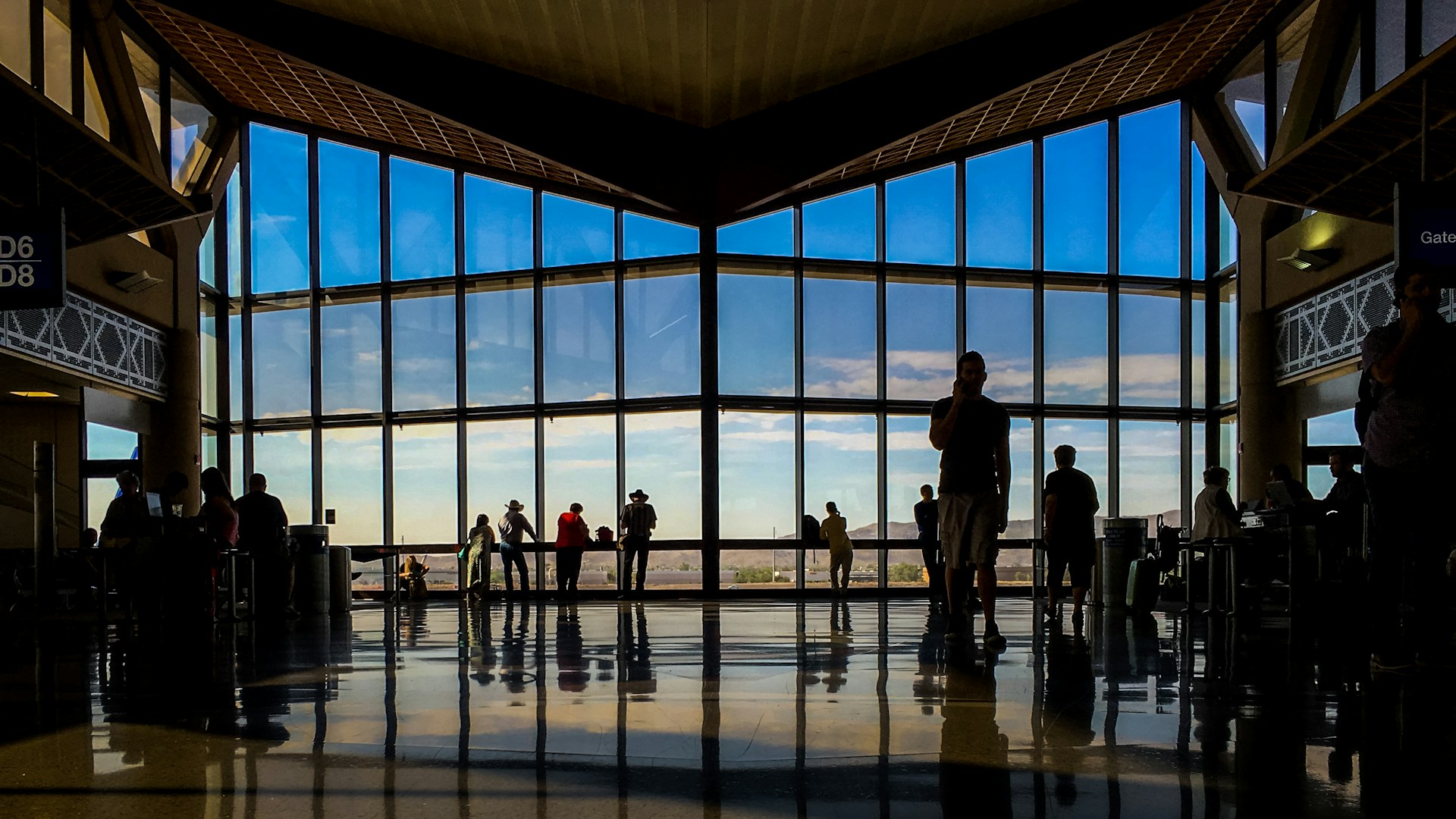 Passengers are pictured inside a naturally lit airport with large glass windows, which reveal blue skies in the background.