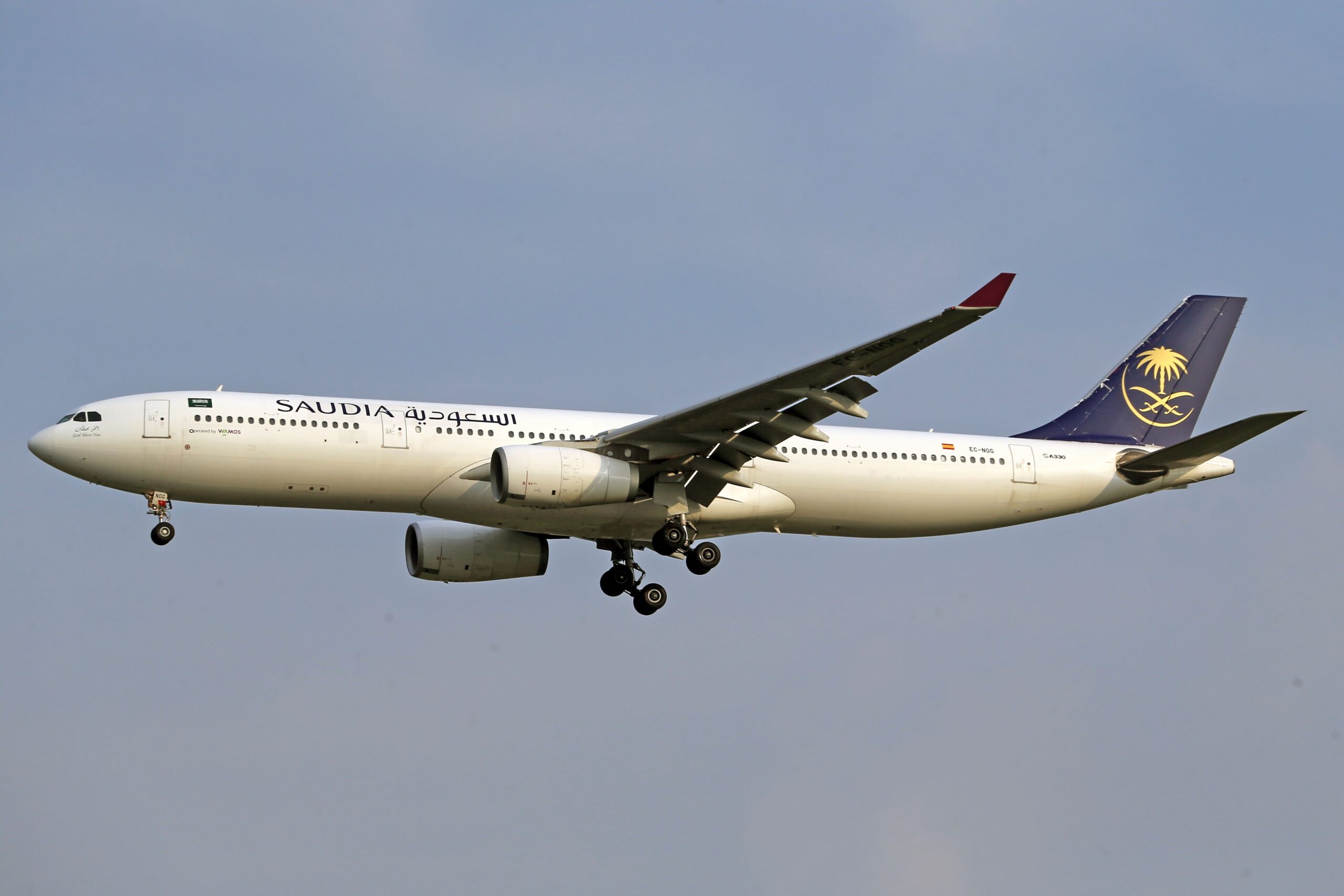 Saudia Airbus A330 captured in mid-air with landing gear deployed against a clear sky.