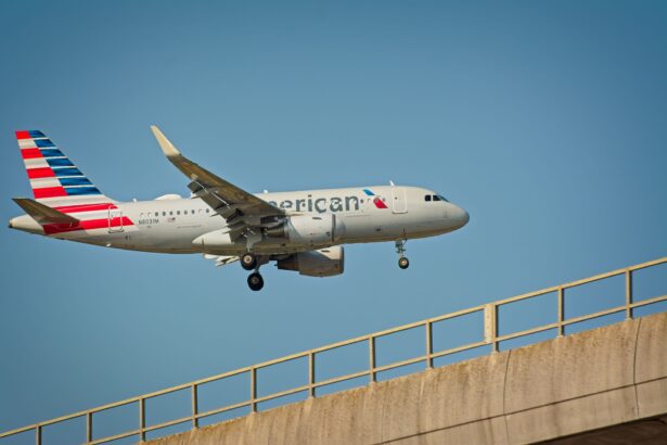 A large American Airlines airplane soars above a bridge, showcasing its wingspan against a clear blue sky.