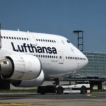 A Lufthansa plane at Frankfurt Airport, featuring terminal structures and a bright blue sky overhead.