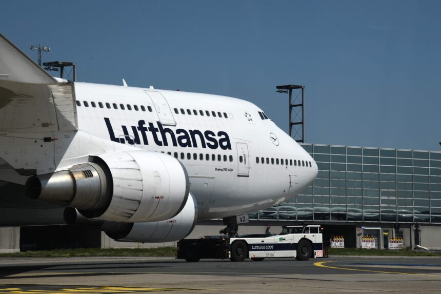 A Lufthansa plane at Frankfurt Airport, featuring terminal structures and a bright blue sky overhead.