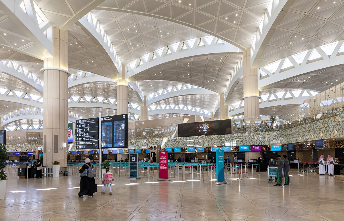 The interior of Riyadh airport. Several check-in desks can be seen as well as gate directions and a departures board.
