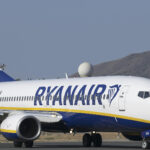 A Ryanair Boeing 737 that has touched down on the runway. Its branding is displayed clearly across the aircraft's side and in the background a hill can be seen along with a blue/grey sky.