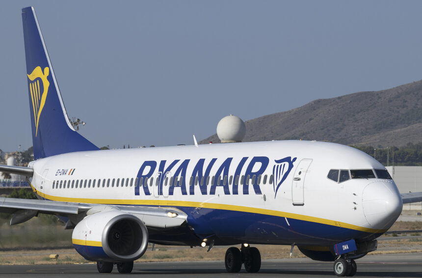 A Ryanair Boeing 737 that has touched down on the runway. Its branding is displayed clearly across the aircraft's side and in the background a hill can be seen along with a blue/grey sky.