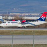 Air Serbia plane pictured landing on an airport runway with grass and trees in the background.