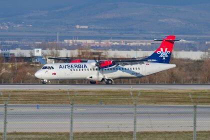 Air Serbia plane pictured landing on an airport runway with grass and trees in the background.