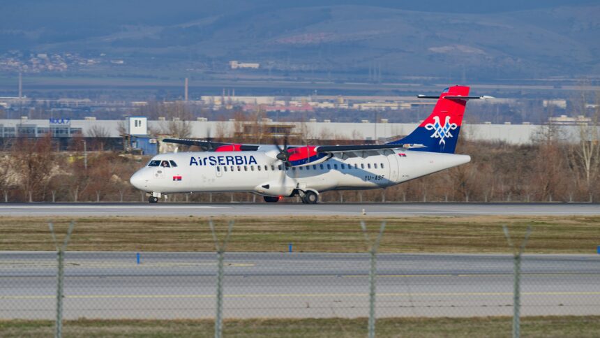 Air Serbia plane pictured landing on an airport runway with grass and trees in the background.