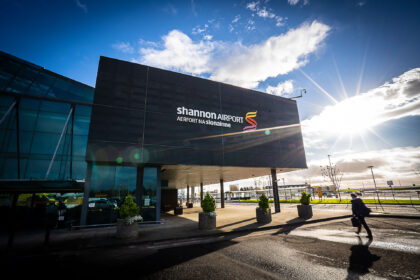 Image shows the exterior of Shannon Airport in Ireland with logo, passengers and sunshine