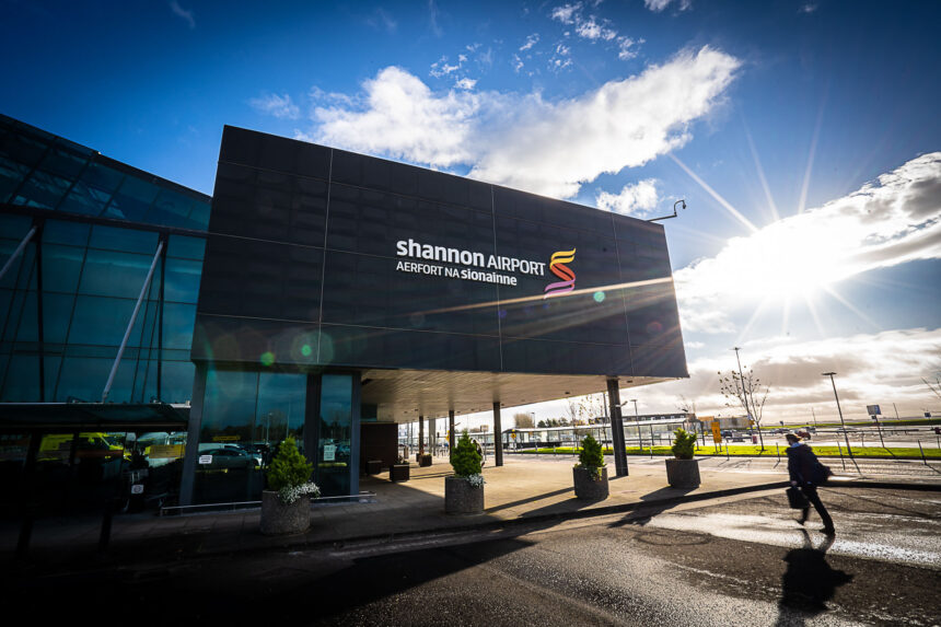 Image shows the exterior of Shannon Airport in Ireland with logo, passengers and sunshine