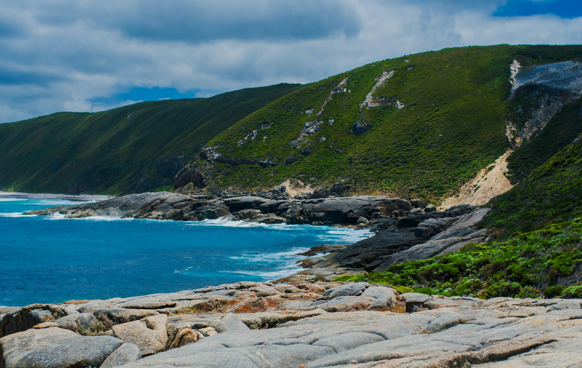 A beach with a body of water and rocks and mountains behind it